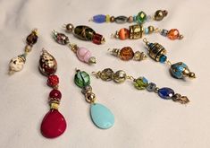 many different colored beads and charms on a white surface with one bead dangling from the end