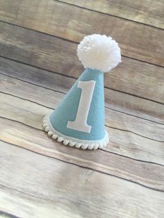 ***Please read shop announcement for current processing times and updates.Your birthday boy will look absolutely adorable in this mini birthday hat for his half birthday or whole birthday!  Perfect for a party or photo shoot. The hat is available in 2 sizes, Mini which is 5 inches tall and 4 inches wide or Full size which is 7 inches tall by 5 inches wide.It features baby blue felt with a white number of your choice. White mini pom pom ribbon is attached along the base of the hat with a yarn Pom Cute White Hat For First Birthday, Playful Blue Hat For First Birthday, Playful Blue Hat For Gift, Playful Blue Hats For Gifts, Cute White Hat For Birthday, Playful Blue Hat As A Gift, White Birthday Party Hat Supplies, Playful Blue Hat As Gift, Playful White Party Supplies For First Birthday