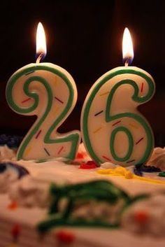 the birthday cake has two candles on it and is decorated with green numbers that read 26