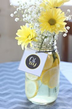 a mason jar filled with lemons and daisies on top of a blue table cloth