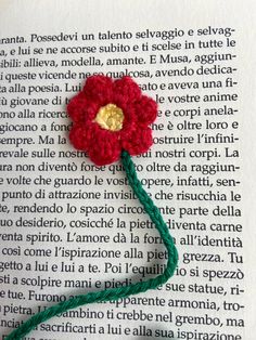 a crocheted red flower sitting on top of an open page of a book