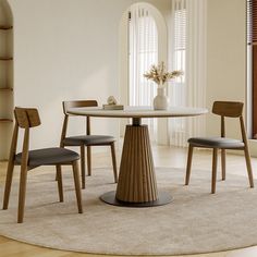 a round table with four chairs around it and a vase on the top, in front of a window