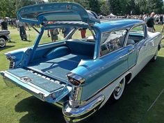 an old blue car parked on top of a lush green field next to other cars