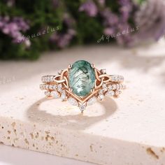 a ring with an oval green stone surrounded by smaller round diamonds on top of a piece of white marble