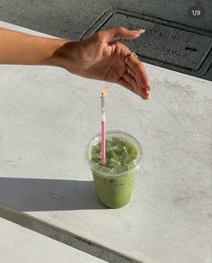 a hand holding a straw over a green smoothie in a plastic cup on a table