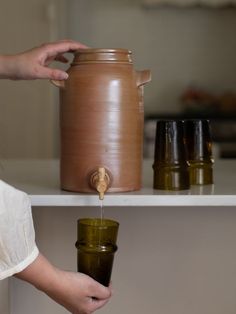 a person pouring something into a cup on top of a shelf next to other jars