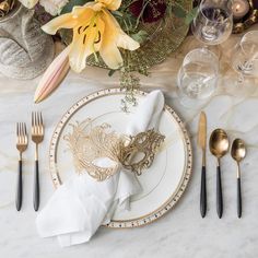 a table set with black and gold place settings, napkins, silverware and flowers