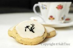 two cookies with icing on them sitting next to a tea cup and saucer