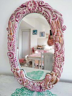 a pink mirror sitting on top of a table next to a white chair and wall