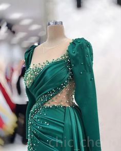 Elevate your evening glam with this exquisite emerald green gown, masterfully designed to make a statement. The dress features a luxurious satin fabric that drapes elegantly over the body, complemented by intricate beadwork and delicate sequins that add the perfect touch of sparkle. The asymmetrical neckline and sheer illusion mesh panels create a unique and captivating silhouette, making this gown the ultimate choice for any formal occasion.Designed with both style and comfort in mind, the gown boasts puffed sleeves that add a modern twist to the classic design. The fitted bodice is adorned with strategically placed bead accents, ensuring you shine from every angle. The gathered detailing along the waistline enhances your natural curves, creating a flattering and sophisticated shape that’ Emerald Green Gown, Dresses Art, Elegant Gowns, Long Sleeve Evening Gowns, Sequin Prom Dress, Green Gown, Beaded Prom Dress, Patterned Tights, Asymmetrical Neckline