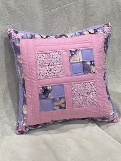 a pink pillow with purple squares and cats on it's sides is sitting on a bed