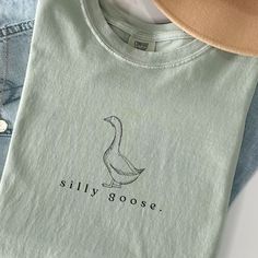 Silly Goose Shirt Silly Goose Tshirt Comfort Colors Silly Goose Vintage Farm Shirt Cute Goose Shirt Gifts for Farm Girls Mom Gifts Homestead This Comfort Colors shirt  features a simplistic graphic of a vintage-style drawing of a goose and the words "silly goose." below. Available in bay, blue jean, white, and mustard. If you are interested in long sleeve, go here: https://withawildflowerllc.etsy.com/listing/1741662335 ✿ The With A Wildflower mission is to give God the glory and give back throug Cute Green Everyday Tops, Cute Everyday Crew Neck Shirt, Cute Goose, Silly Goose, Vintage Farm, Farm Girl, Mom Gifts, Comfort Colors Tee, Girl Mom