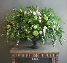 a vase filled with green and white flowers sitting on top of a wooden table next to a wall