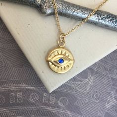 ⇩CLICK BELOW FOR DETAILS⇩Please note that I make every effort to mail your order within 24 hours of receipt. However, USPS is experiencing significant delivery delays and many packages are taking 2-3 weeks to arrive.Made of all 14kt gold filled, this beautiful evil eye necklace has a 11.5mm disc shaped evil eye charm with a tiny and bright faceted synthetic blue sapphire or red ruby center stone.  The charm is identical on both sides, and hangs a jump ring from a delicate 14kt gold filled chain, Gold Plated Evil Eye Symbolic Jewelry, Symbolic Gold Plated Evil Eye Jewelry, Spiritual Tarnish-resistant Round Pendant Charm Necklace, Yellow Gold Evil Eye Spiritual Necklace, Spiritual Yellow Gold Evil Eye Necklace, Spiritual Yellow Gold Necklace With Evil Eye, Symbolic Yellow Gold Evil Eye Necklace, Symbolic Evil Eye Yellow Gold Necklace, Handmade 14k Gold Jewelry For Good Luck