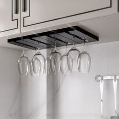 five wine glasses hanging from the ceiling in a kitchen with marble counter tops and white cabinets