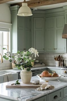 a kitchen with green cabinets and white flowers in a vase on the counter top next to a cutting board