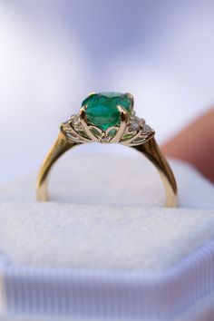 an engagement ring with a heart shaped emerald surrounded by small diamonds on a white box