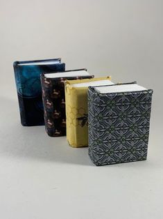 three small notebooks sitting next to each other on a white surface with an intricate pattern