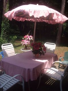 the table is covered by an umbrella with pink flowers on it and blue chairs around it