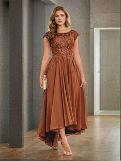 a woman in a brown dress standing on a wooden floor with her hands in her pockets