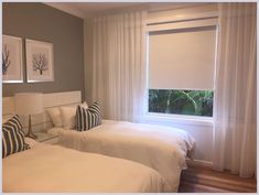 two beds in a room with white sheets and pillows, one is next to the window