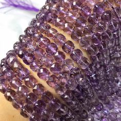 a close up view of purple beads on a woman's arm with feathers in the background