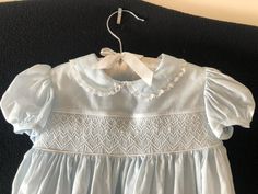 This 12 month size baby dress is made from a special fabric from Switzerland, Swiss Nelona. It is very soft and perfect for that special baby. It is hand smocked with white cotton floss and the smocked insert is bordered with handmade blue mini piping. It has gathered lace on the collars and a double row of lace on the hem. It closes with three small buttons on the back. It measures 16' from the nape of the neck to the bottom of the hem. Cotton Smocked Dress With Ruffles For Baptism, Elegant Smocked Ruffle Dress For Baptism, Elegant Smocked Dress With Smocked Cuffs For Baptism, Fitted Smock Baptism Dress For Spring, Cotton Baptism Dress With Smocked Bodice, Cotton Dress With Smocked Bodice For Baptism, Fitted Light Blue Smocked Cotton Dress, Light Blue Fitted Smocked Cotton Dress, Light Blue Fitted Cotton Smocked Dress