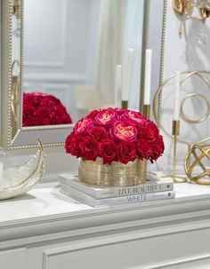 a white dresser topped with pink roses and candles next to a mirror filled with books