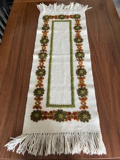 a table runner with flowers and fringes on it sitting on top of a wooden table