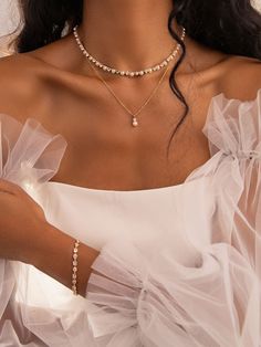 a woman in a white dress wearing a necklace and bracelet with pearls on the neck