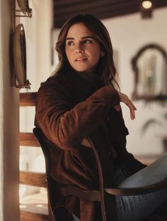 a woman sitting in a chair with her hand on the back of her shoulder and looking off into the distance