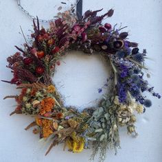 a dried wreath hanging on the side of a white wall next to a metal hook