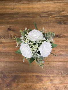 a bouquet of white roses and greenery on a wooden surface