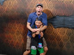 a man holding a child in his arms while standing next to a wall with an animal on it