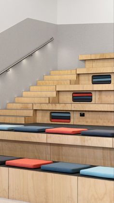 rows of wooden benches with blue and red cushions on them in front of a stair case