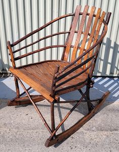 a wooden rocking chair sitting in front of a metal wall with a shadow on the ground