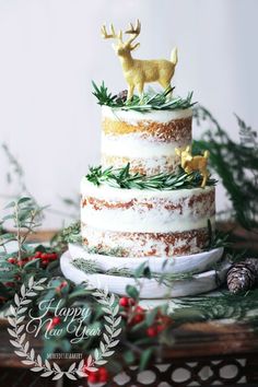 a three tiered cake decorated with greenery and gold deer figurines on top