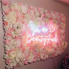 a flower wall with the words you are beautiful written in neon letters on it and surrounded by flowers