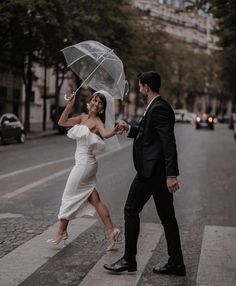 a bride and groom crossing the street with an umbrella