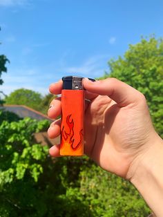 a hand holding an orange lighter in front of trees