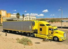 a large yellow semi truck parked in a parking lot next to a building and palm trees