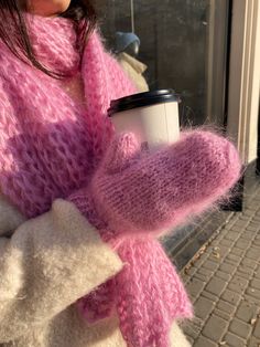 a woman holding a cup of coffee wearing a pink knitted scarf and mittens