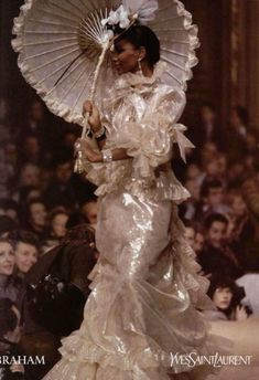 a woman is walking down the runway in a white dress with an open parasol