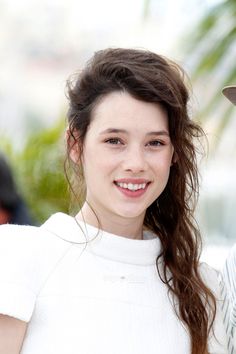 a woman with long brown hair wearing a hat and white dress smiling at the camera