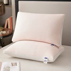 a close up of a pillow on a bed near a table with a book and lamp