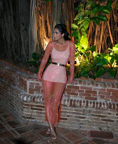 a woman in a pink dress standing next to a brick wall