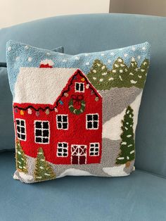 a blue couch with a red house on it's side and christmas trees in the back