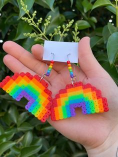 a pair of rainbow earrings is shown in front of a plant with green leaves on it