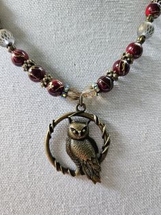 47mm antique bronze metal focal owl. 10mm burgundy with bronze drizzle acrylic rounds. 10mm frosted glass rounds with an etched diamond pattern. 8mm bumpy metal rondelles. 8mm antique bronze rondelles with crystals. 6mm crystal bicones in honey. Antique bronze toggle clasp. Antique Gold Beaded Jewelry With Round Beads, Bronze Beaded Round Necklaces, Round Bronze Beaded Necklaces, Bronze Metal Necklace With Round Beads, Brass Spacer Beads Jewelry, Antique 8mm Beads For Jewelry Making, Bronze Czech Glass Necklace For Jewelry Making, Red Brass Jewelry With Round Beads, Bronze Round Bead Copper Jewelry