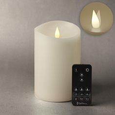 a remote control next to a lit candle on a gray surface with two lights in the background